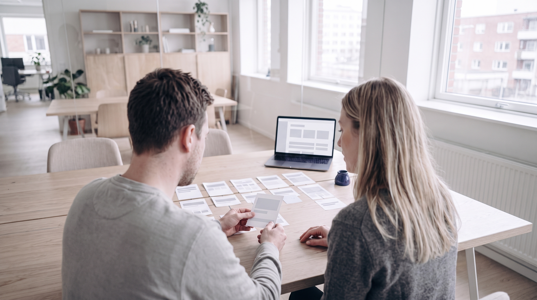 Two people review prepared cards together at a light wooden table; one card is set aside for human review.